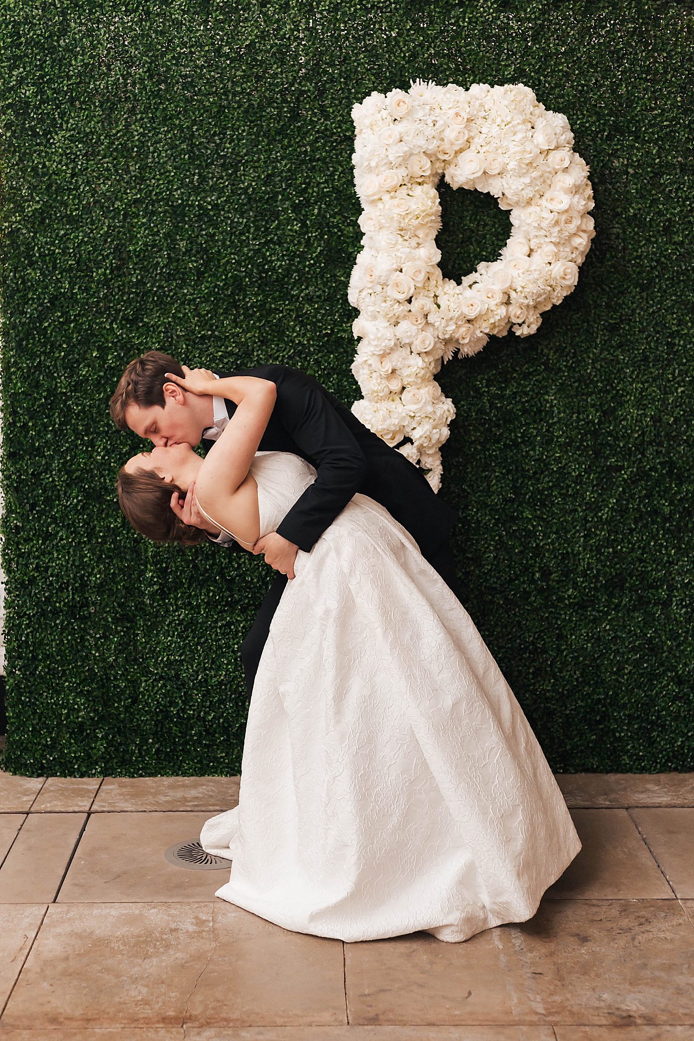 Bride and groom kissing in front of greenery wall | Carters Event Co