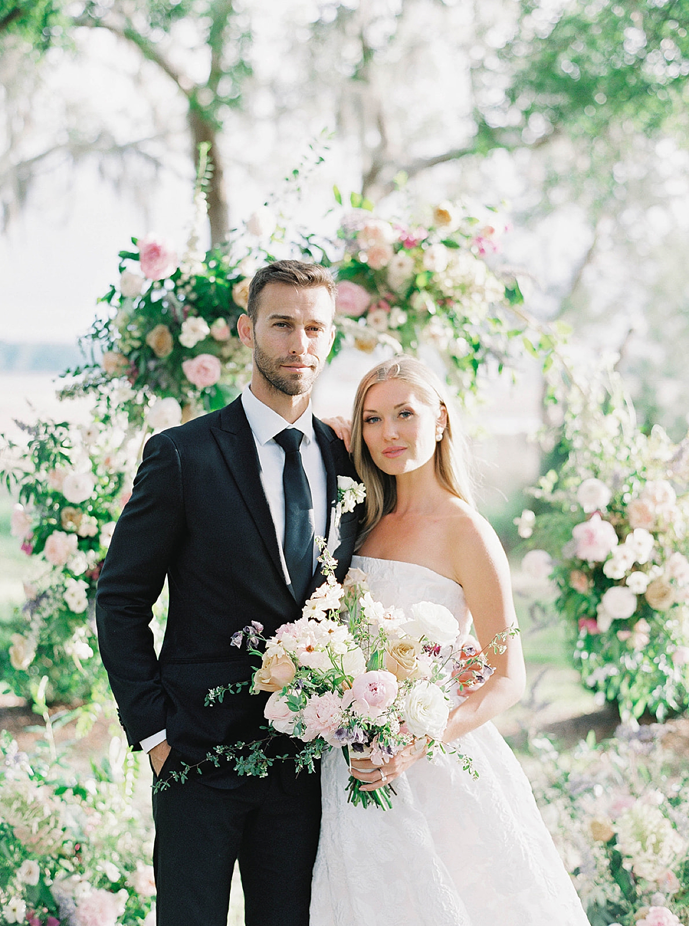 Bride and groom posing in front of floral arbor | Carters Event Co